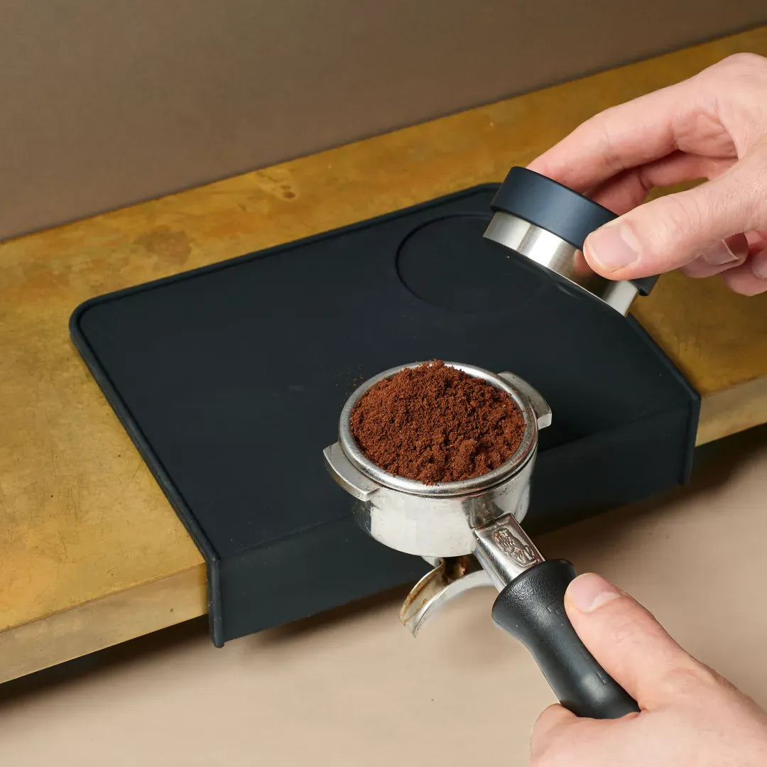 JoeFrex Tampingmatte im Einsatz – Barista tampt frisch gemahlenen Kaffee im Siebträger für Espresso
